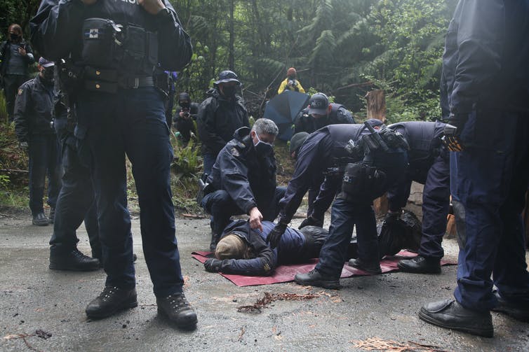 A man lies face down on the ground while police kneel next to him.