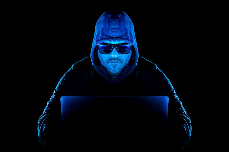a man wearing a hooded sweatshirt and sunglasses types on a laptop computer