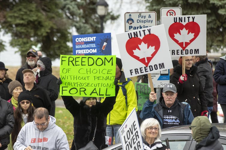 a group of anti-vaccine mandate protestors holding signs that read UNITY FREEDOM and FREEDOM OF CHOICE FOR ALL