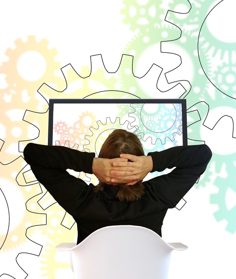 A man sits in front of a desktop computer with a mural of gears in the background.