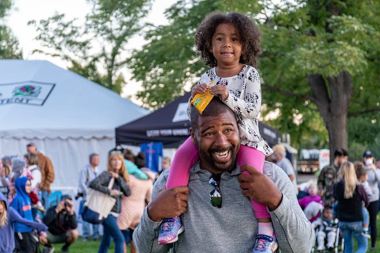 A little girl is seen sitting on her father's shoulders.