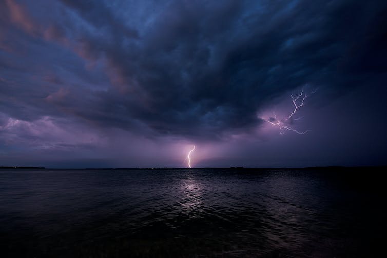 a bolt of lightning can be seen on the horizon in the clouds above the sea
