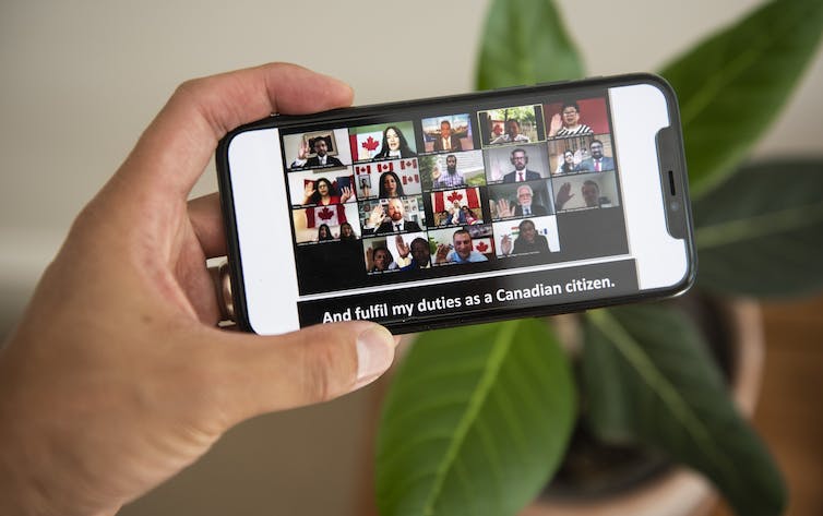 A grid of people raise their hands during a virtual citizenship ceremony as seen on a mobile phone screen