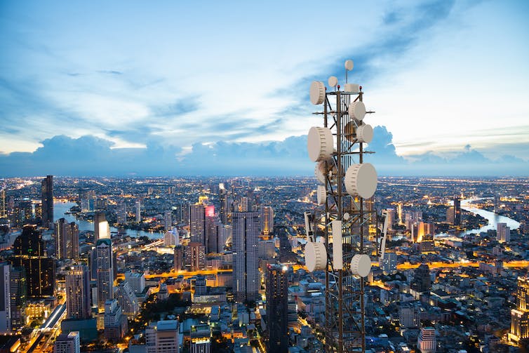 Telecommunication tower with 5G cellular network antenna on city skyline background.