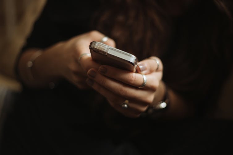 A person with painted nails and rings holds a mobile phone.