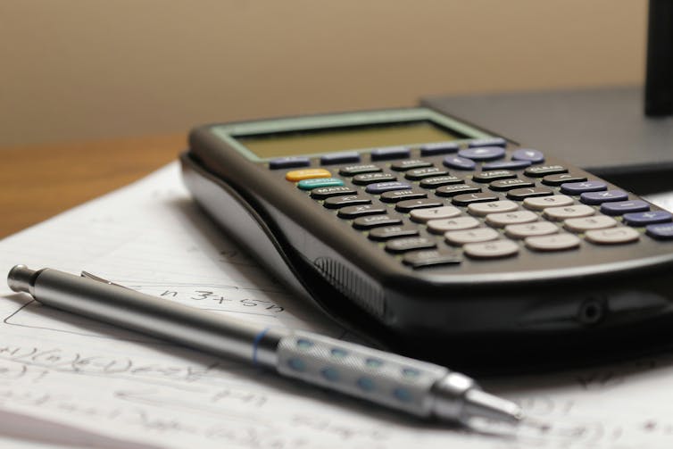 A calculator and pen rest on a notebook.