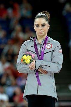 Young woman scrunches her mouth as she holds a small bouquet of flowers and folds her arms.