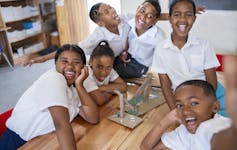School children laughing and pulling faces around an item they have made from cardboard