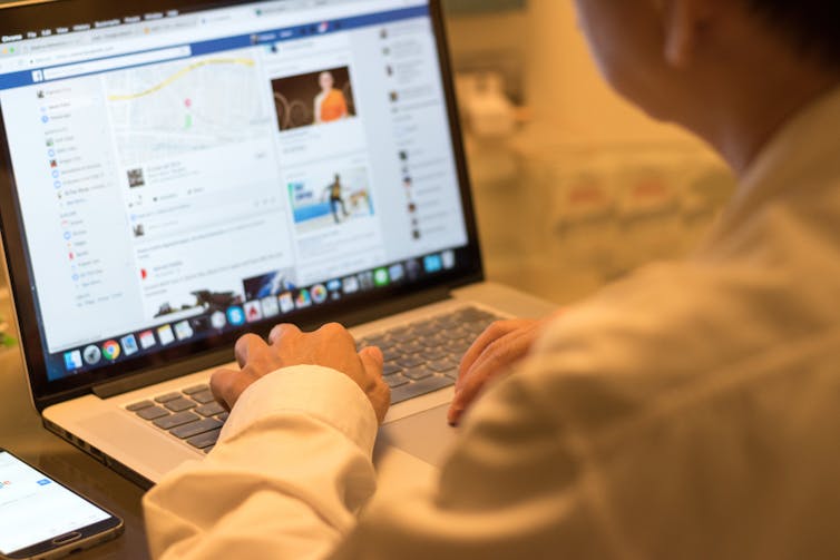 Person sitting at a table using Facebook on a laptop.